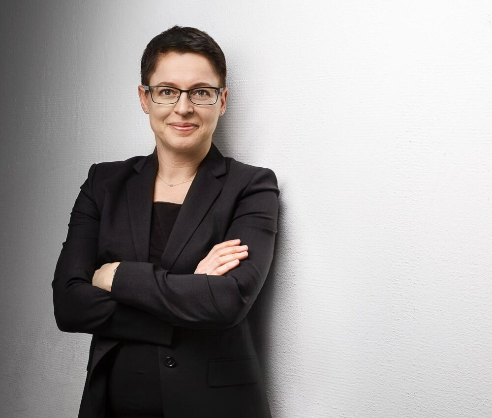 Businessfotografie Luzern - Frau in schwarzem Anzug und Brille vor weisser Wand