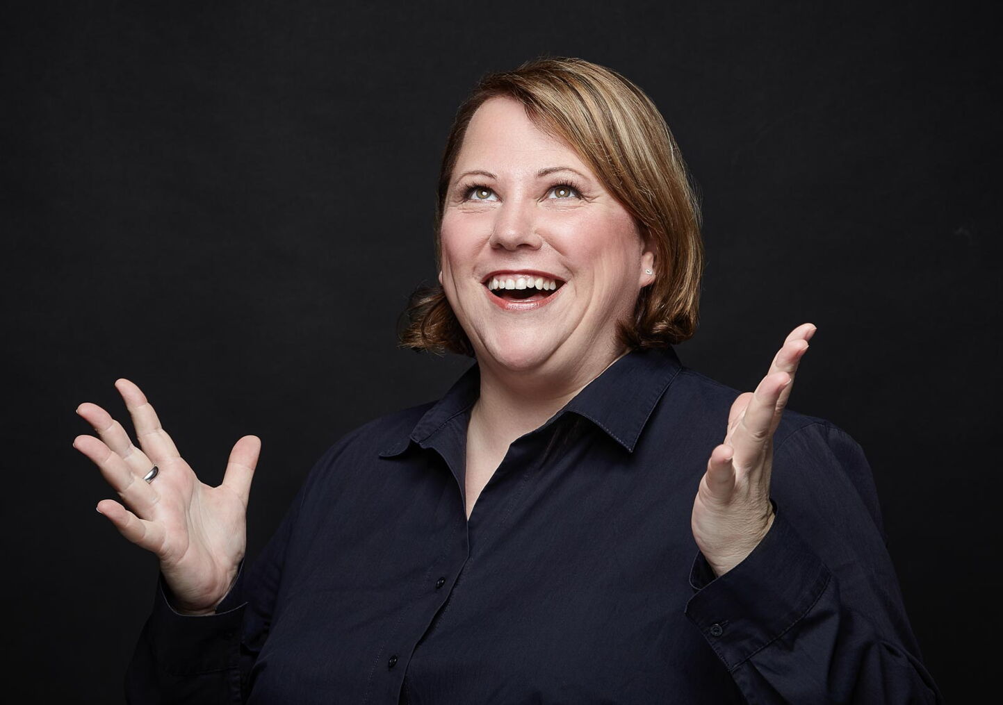 Businessfotografie: Frau in dunkelblauem Hemd vor schwarzem Hintergrund mit freudigem Ausdruck