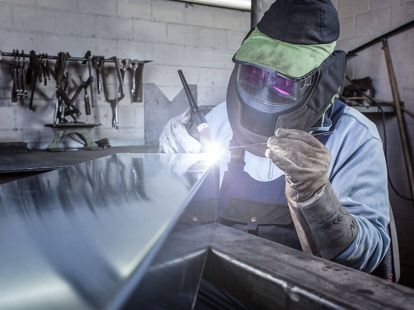 Industriefotograf Luzern - Aluminiumschweissen Spenglerei Arbeiten Industriefotograf Luzern - Schweisser mit Schutzanzug schweisst ein Aluminiumstück auf Werkbankkonsolen